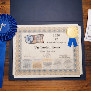 May include: A blue ribbon with gold text reading "1st" and "23rd World Leather Debut 2026 Best of Category" sits next to a certificate. The certificate is for "Un-Tooled Items" and includes a gold seal.