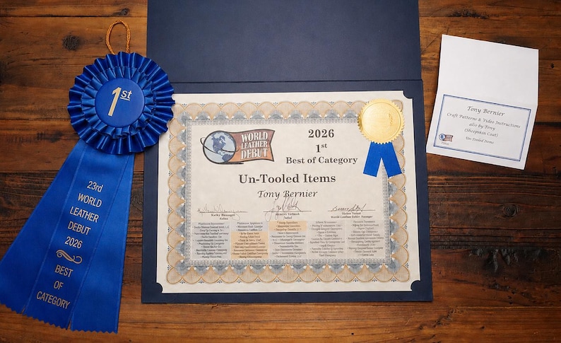 May include: A blue ribbon with gold text reading "1st" and "23rd World Leather Debut 2026 Best of Category" sits next to a certificate. The certificate is for "Un-Tooled Items" and includes a gold seal.