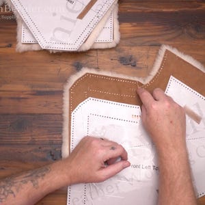 May include: A person's hands are working with leather and paper patterns on a wooden surface. The leather is brown with a white, fluffy edge. The paper patterns are white with dotted lines and text. The text includes "Front Left Top".
