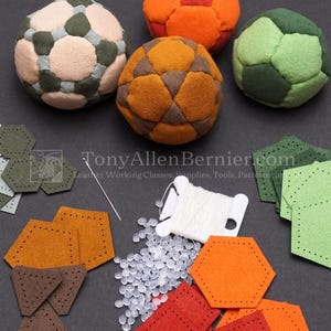 May include: A DIY craft kit featuring three finished multi-colored fabric balls, assorted pre-cut geometric leather pieces in shades of green, orange, and brown, a sewing needle, white thread, and clear plastic pellets. Text reads TonyAllenBernier.com.
