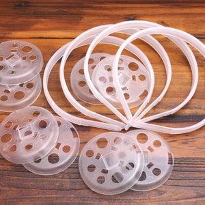 May include: A set of clear plastic headband holders with a circular design and multiple holes. The holders are designed to keep headbands organized and prevent them from getting tangled.