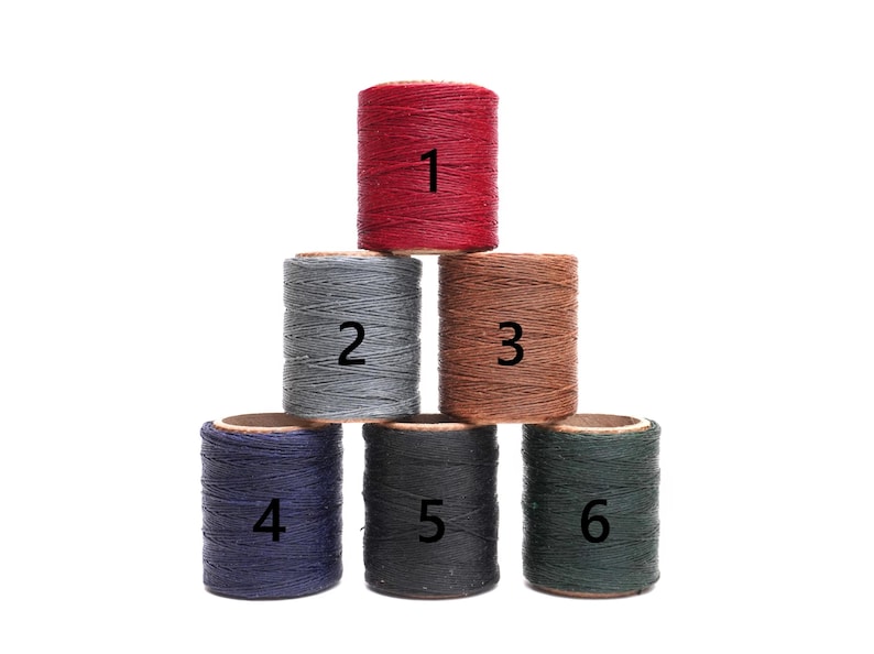 Op de afbeelding: Zes spoelen met gewaxt garen in verschillende kleuren, genummerd van 1 tot en met 6. De spoelen zijn in een piramidevorm gerangschikt.