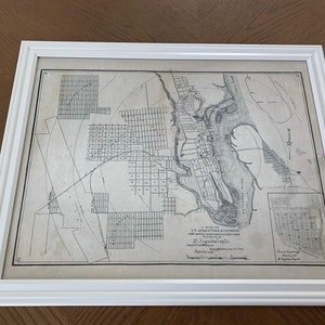 May include: A black and white map of the city of Alexandria, Virginia, from 1854. The map shows the city's streets, buildings, and waterways. The title of the map is "A Map of the City of Alexandria, Virginia, with its Environs, Compiled from Actual Surveys, by J.H. Alexander, 1854."