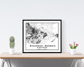 Könnte beinhalten: Schwarz-weiß-Linienkunst-Kartenabdruck von Savannah, Georgia und Umgebung. Der Druck ist in einem schwarzen Rahmen gerahmt und auf einem Holztisch mit einem Kaktus und rosa Blumen in weißen Töpfen ausgestellt.