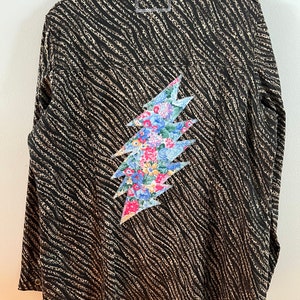 May include: A black and brown long-sleeved shirt with a floral patterned lightning bolt design on the back.