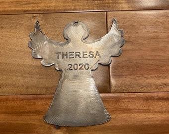 May include: A silver metal angel ornament with the name "THERESA" and the year "2020" engraved on it.