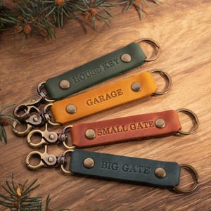 May include: Four leather keychains with metal key rings. The keychains are labelled "House Key", "Garage", "Small Gate", and "Big Gate".
