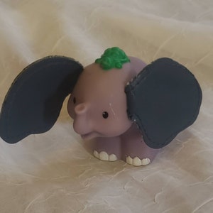 May include: A purple elephant toy with large grey ears and a green leaf on its head. The toy has a simple, cartoon-like design.
