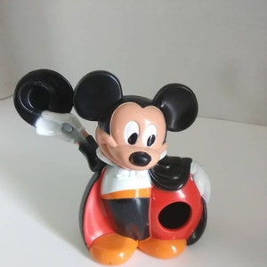 Peut inclure: Une figurine en plastique de Mickey Mouse noire et rouge portant une cape et tenant un chapeau haut de forme. La figurine a un trou à l'arrière de la tête.