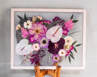 May include: A framed pressed flower arrangement with a variety of pink, purple, and white flowers. The flowers are arranged in a bouquet shape and are pressed between two pieces of glass.