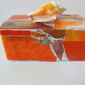 May include: Orange and brown mosaic glass box with a seashell on top and a gold latch.