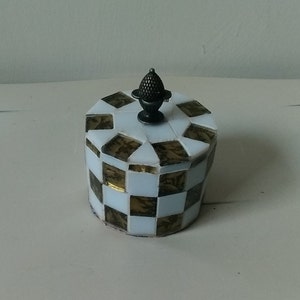 May include: A small, round, white and gold mosaic box with a black metal knob on top.