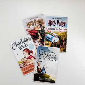 May include: Four paperback books stacked on a white surface. The top book is "Harry Potter and the Chamber of Secrets, Part 2" by J.K. Rowling. The second book is "Harry Potter and the Philosopher's Stone" by J.K. Rowling. The third book is "Charlotte's Web" by E.B. White. The bottom book is "The Green Ember" by S.D. Smith.