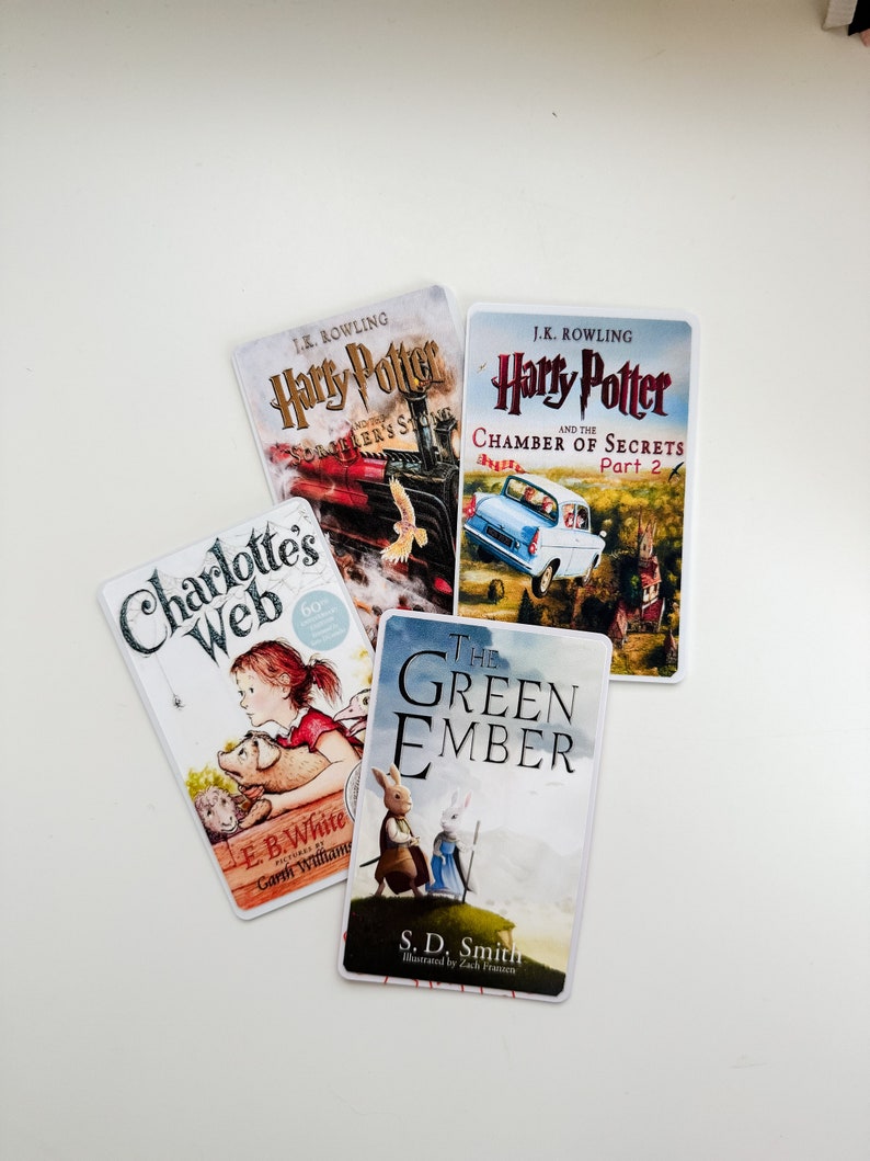 May include: Four paperback books stacked on a white surface. The top book is "Harry Potter and the Chamber of Secrets, Part 2" by J.K. Rowling. The second book is "Harry Potter and the Philosopher's Stone" by J.K. Rowling. The third book is "Charlotte's Web" by E.B. White. The bottom book is "The Green Ember" by S.D. Smith.