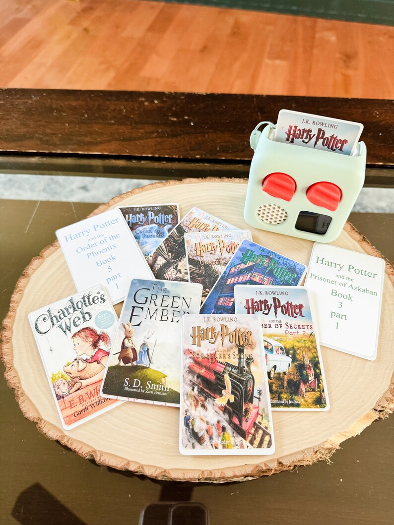 May include: A collection of book covers featuring popular children's and young adult novels, including Harry Potter and the Order of the Phoenix, Harry Potter and the Prisoner of Azkaban, Charlotte's Web, and The Green Ember. The covers are arranged on a wooden surface.