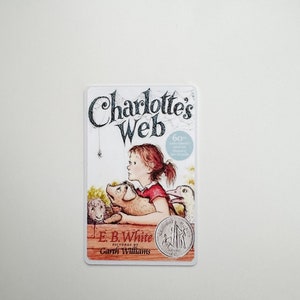 May include: A book cover for Charlotte's Web by E.B. White, illustrated by Garth Williams. The cover features a young girl with a pig, a lamb, and a spider.
