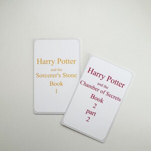 May include: Two white cards with gold and red text. The first card says "Harry Potter and the Sorcerer's Stone Book 1". The second card says "Harry Potter and the Chamber of Secrets Book 2 part 2".