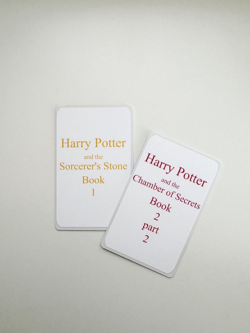 May include: Two white cards with gold and red text. The first card says "Harry Potter and the Sorcerer's Stone Book 1". The second card says "Harry Potter and the Chamber of Secrets Book 2 part 2".