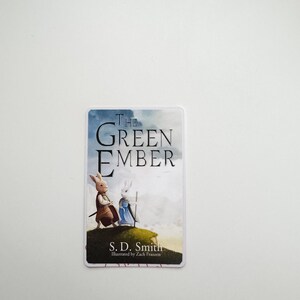 May include: A book cover with a white background and blue clouds. The title "The Green Ember" is in black text. Two white rabbits are walking on a green hill. The author is S.D. Smith and the illustrator is Zach Franzen.