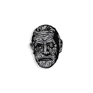 Puede incluir: Pin de esmalte en blanco y negro con una ilustración detallada de la cara de un hombre con un solo ojo.