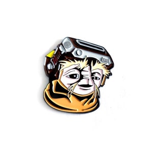 May include: A brown and yellow enamel pin featuring a cartoon character with a large head, brown hair, and a white face. The character is wearing a brown and silver helmet with a yellow visor. The pin is a popular character from the 1980s movie, "Labyrinth".