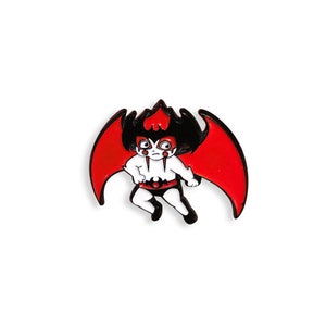 May include: A red and black enamel pin featuring a cartoon devil with wings. The devil is wearing a black and red outfit and has a black and white face.