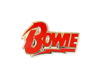 Puede incluir: Pin de metal rojo y dorado con la palabra "BOWIE" en una fuente estilizada.
