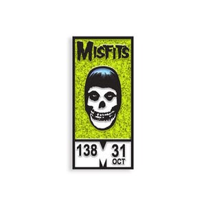 Op de afbeelding: Een ingelijste print met het woord "MISFITS" in groen en zwart, boven een zwart-witte schedelafbeelding. De onderkant van de print toont de cijfers "138 31 OKT" in een witte doos.