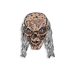 May include: A pin depicting a ghoulish face with blue eyes, a wrinkled forehead, and long white hair. The face has a skeletal appearance with a sinister grin. The pin is likely made of metal and is a collectible item.