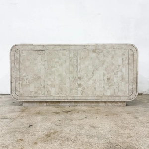 May include: A light-colored, rectangular cabinet with a mosaic-like pattern. The cabinet has four doors and rounded edges. It sits on a low, rectangular base. The overall design is neutral and modern.