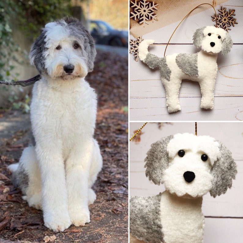 Pode incluir: Um c&atilde;o fofo, branco e cinzento, sentado ao ar livre, com uma trela. A imagem tamb&eacute;m mostra um enfeite de c&atilde;o de feltro com manchas cinzentas e brancas, e um close-up do rosto do enfeite. O enfeite tem um fio dourado para pendurar.