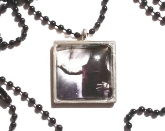 May include: A black chain necklace with a square pendant featuring a black and white photo of a person. The pendant has a silver frame.
