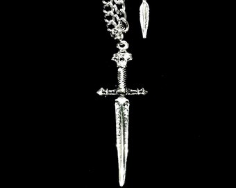 May include: A silver-colored pendant necklace featuring a detailed sword design. The sword hangs from a chain with a feather charm. The necklace is set against a black background.