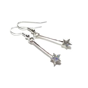 May include: A pair of silver dangle earrings with a star-shaped charm. The star is covered in iridescent glitter.