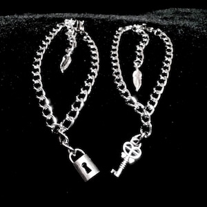 May include: Two silver chains with a lock and key pendant. The chains are linked together and have small feather charms hanging from them.