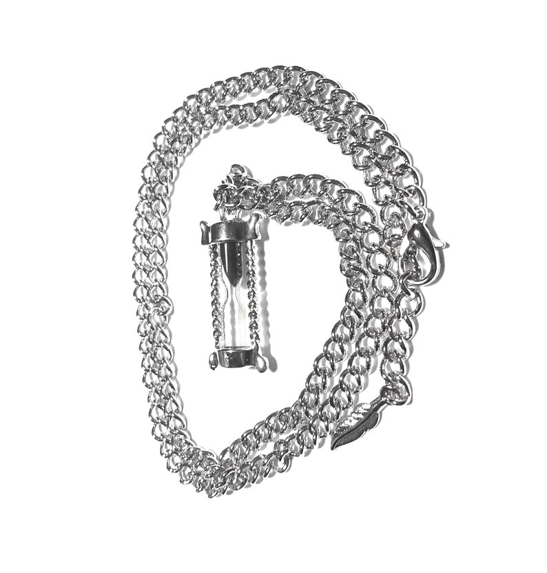 May include: A silver chain necklace with an hourglass pendant. The hourglass is filled with clear sand and has a silver frame.
