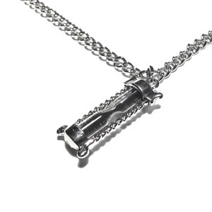 May include: A silver chain necklace with an hourglass pendant. The hourglass is made of metal and has a detailed design.