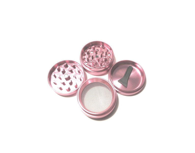 K&ouml;nnte beinhalten: Ein rosa Metall-Grinder mit vier Teilen. Der Grinder hat ein Sieb, ein Fach f&uuml;r Kr&auml;uter, ein Fach f&uuml;r Kief und einen Schaber.