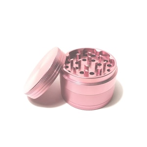 K&ouml;nnte beinhalten: Ein rosa Metall-Grinder mit vier Abschnitten. Der obere Abschnitt hat eine Reihe von L&ouml;chern zum Mahlen von Kr&auml;utern. Der Grinder ist offen und der obere Abschnitt ist abgenommen.