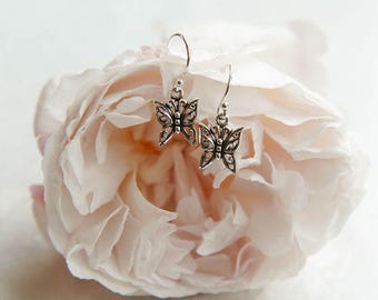 Könnte beinhalten: Silberne Schmetterlings-Ohrringe mit filigranen Details, die auf einer weichen, hellrosa Rose liegen.