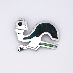 May include: A silver brooch in the shape of a stylized bird with green enamel accents.