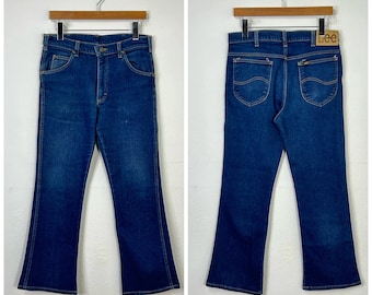 May include: A pair of blue denim jeans with a wide leg opening. The jeans have a brown leather patch with the word "Lee" on the back right pocket.