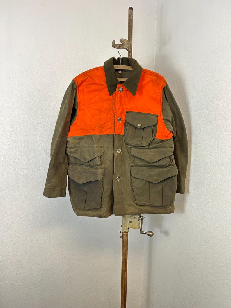 May include: A green and orange hunting jacket with multiple pockets. The jacket has a button closure and a corduroy collar.