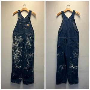 May include: A pair of blue denim overalls with white paint splatters. The overalls have adjustable straps and multiple pockets.
