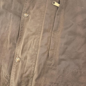 Peut inclure: Gros plan sur une veste marron avec une fermeture &eacute;clair et deux boutons. La veste a une poche sur le c&ocirc;t&eacute; droit et est faite d'un mat&eacute;riau durable. Les boutons ont un design circulaire.