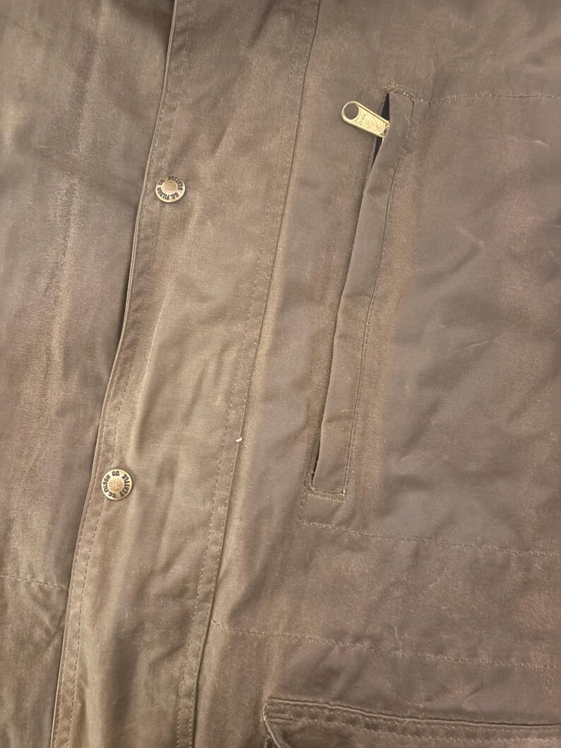 Peut inclure: Gros plan sur une veste marron avec une fermeture &eacute;clair et deux boutons. La veste a une poche sur le c&ocirc;t&eacute; droit et est faite d'un mat&eacute;riau durable. Les boutons ont un design circulaire.