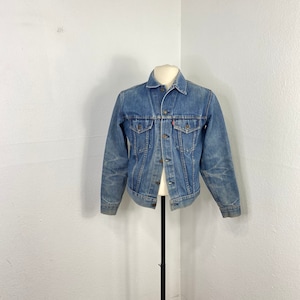 May include: A blue denim jacket with a button closure and two front pockets. The jacket is on a mannequin and has a faded look.