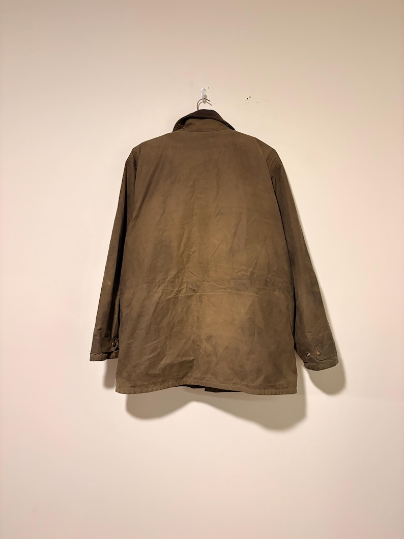 Peut inclure: Veste marron avec un col marron fonc&eacute; suspendue &agrave; un crochet en m&eacute;tal. La veste a un devant boutonn&eacute;, des manches longues et une taille &agrave; cordon. La veste est faite d'un mat&eacute;riau durable et r&eacute;sistant &agrave; l'eau.