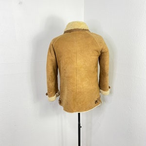 May include: A brown sheepskin jacket with a white shearling collar and lining. The jacket has a zipper closure and two pockets on the front.