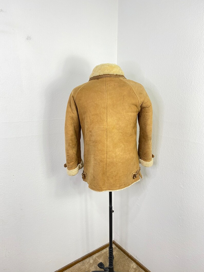 May include: A brown sheepskin jacket with a white shearling collar and lining. The jacket has a zipper closure and two pockets on the front.